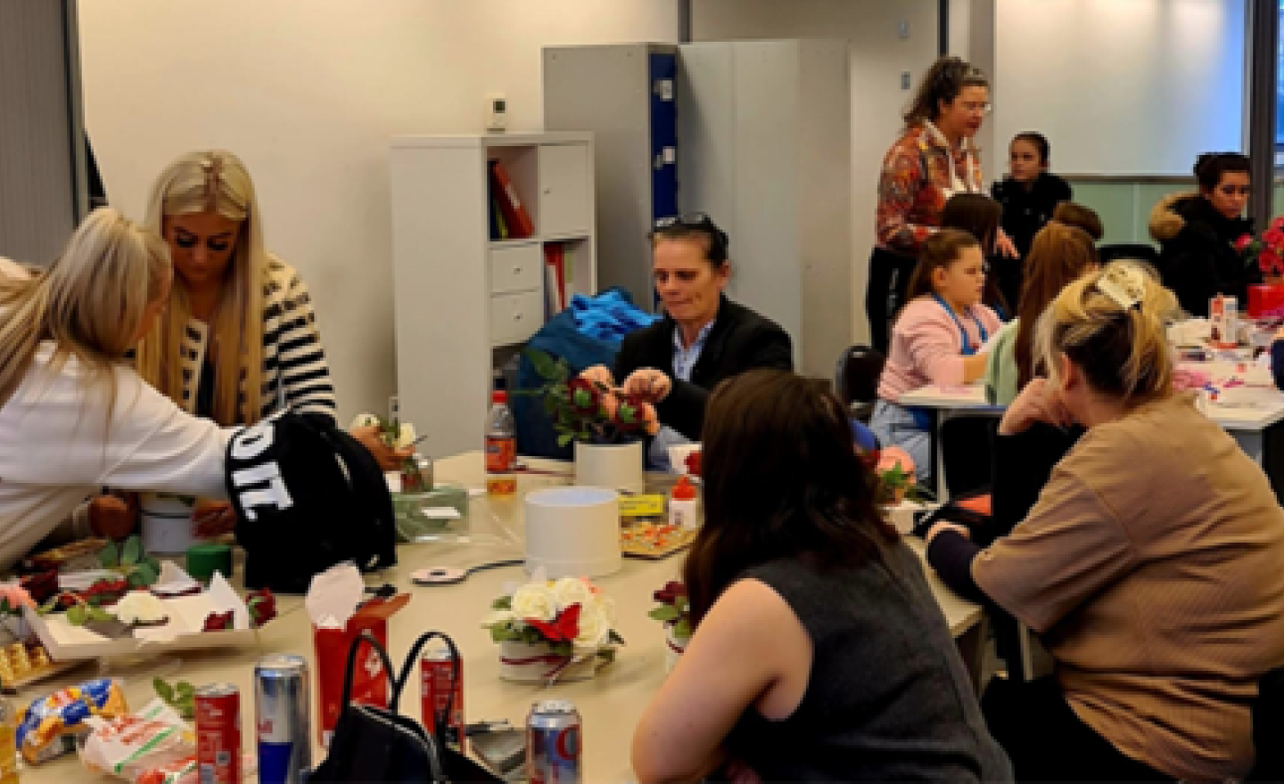 A group of people sitting across two tables engaged in a floral arrangement activity.