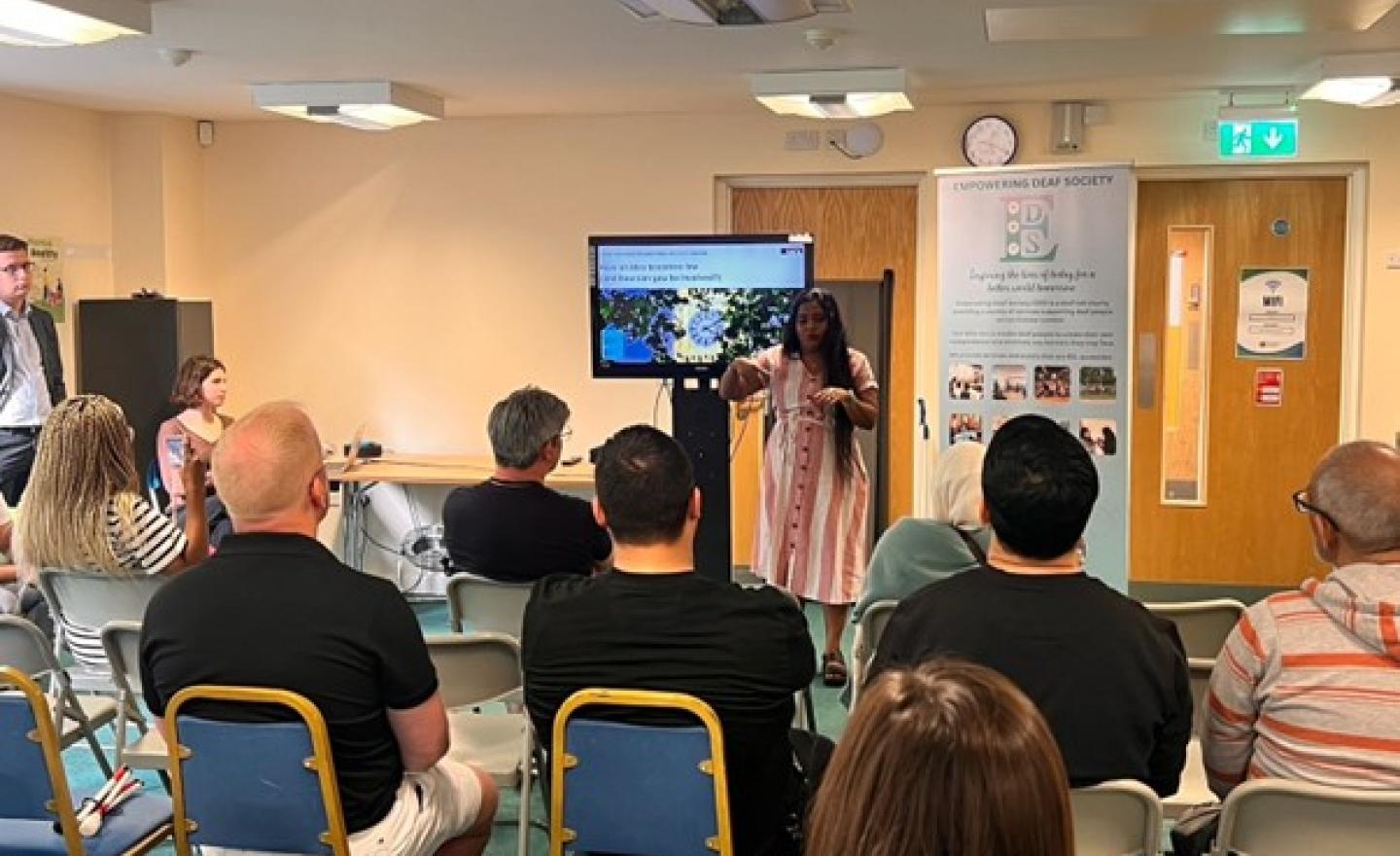 Person delivering civic and democratic participation workshop in BSL to a room of seated participants
