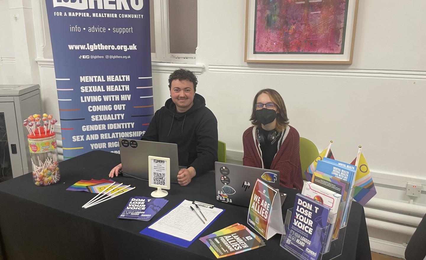 Two LGBT HERO staff sitting behind a stall with information on civic and democratic participation for the LGBTQIA+ communities