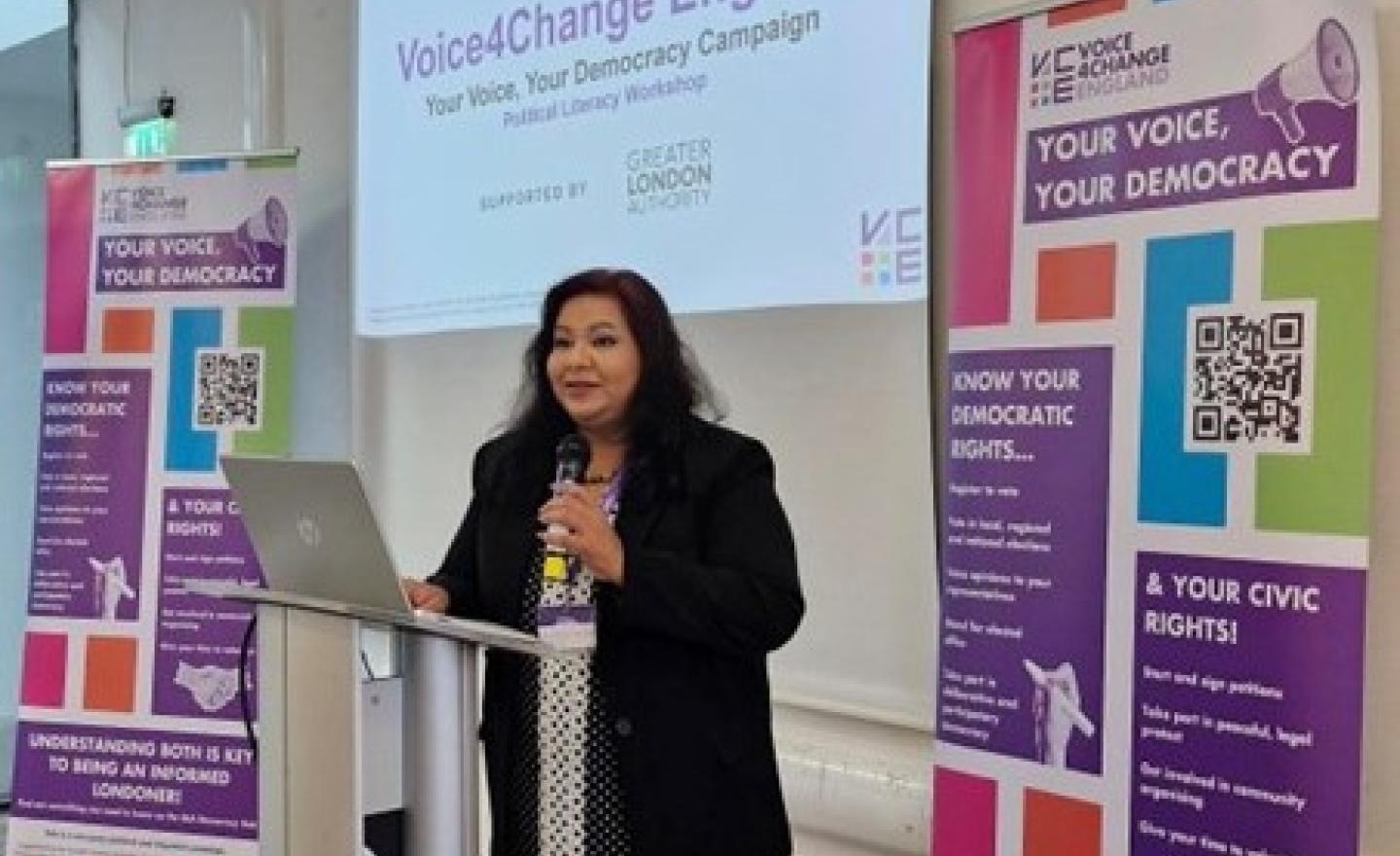 A women standing in front of a presentation screen delivering a civic and democratic participation workshop