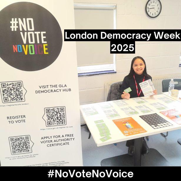 Woman sat behind a table with resources about registering to vote, photo Voter ID and civic participation.