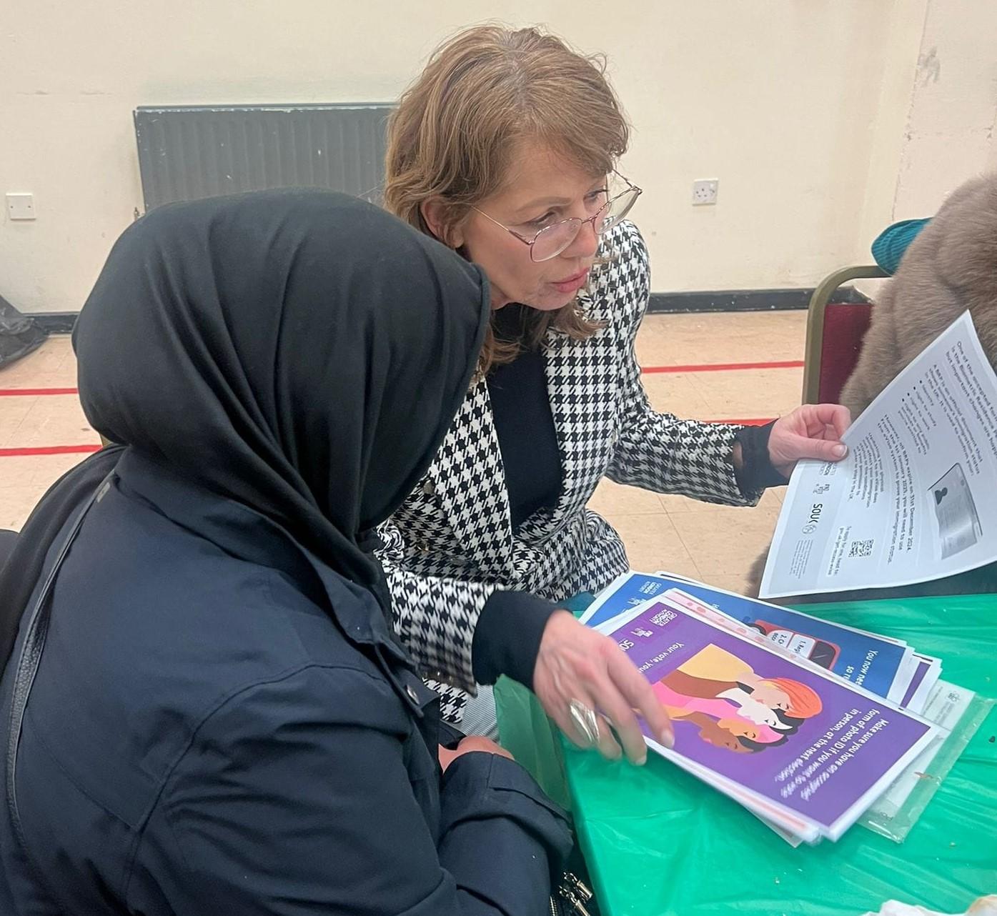 Two women, one talking to the other about registering to vote and civic and democratic participation
