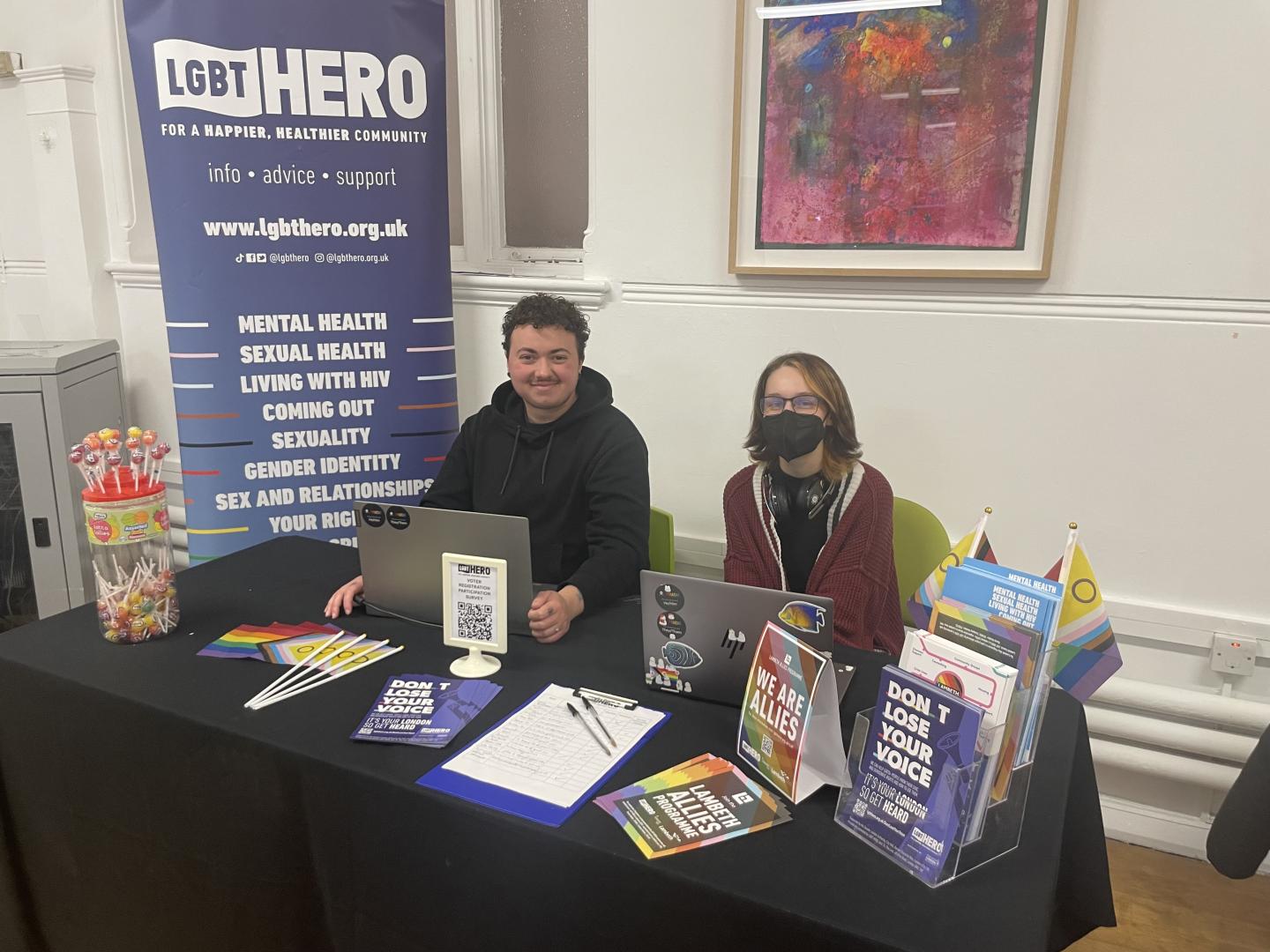 Two LGBT HERO staff sitting behind a stall with information on civic and democratic participation for the LGBTQIA+ communities