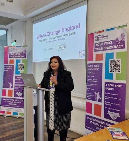 A women standing in front of a presentation screen delivering a civic and democratic participation workshop